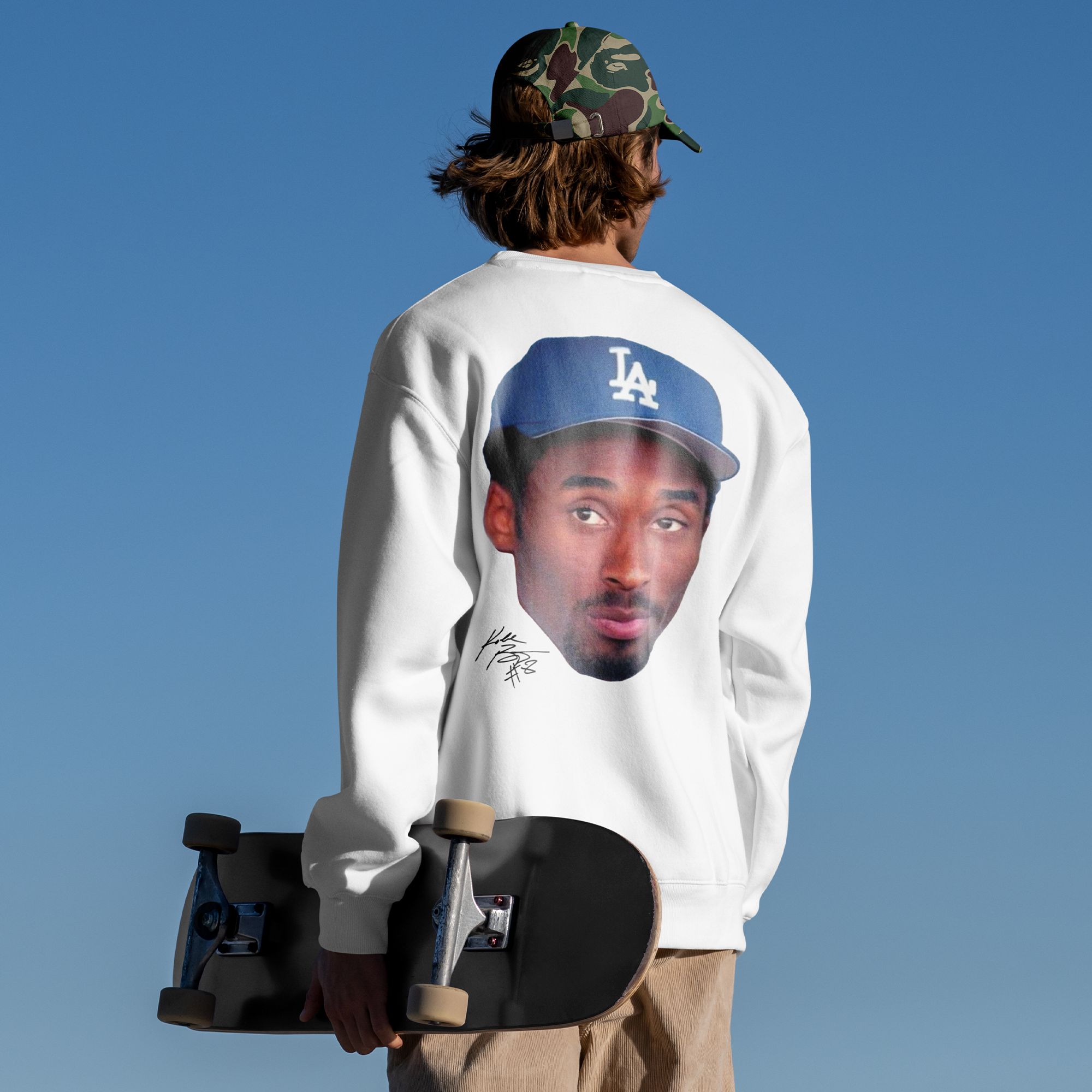 Person wearing a sweatshirt with a graphic design, holding a skateboard against a clear blue sky.