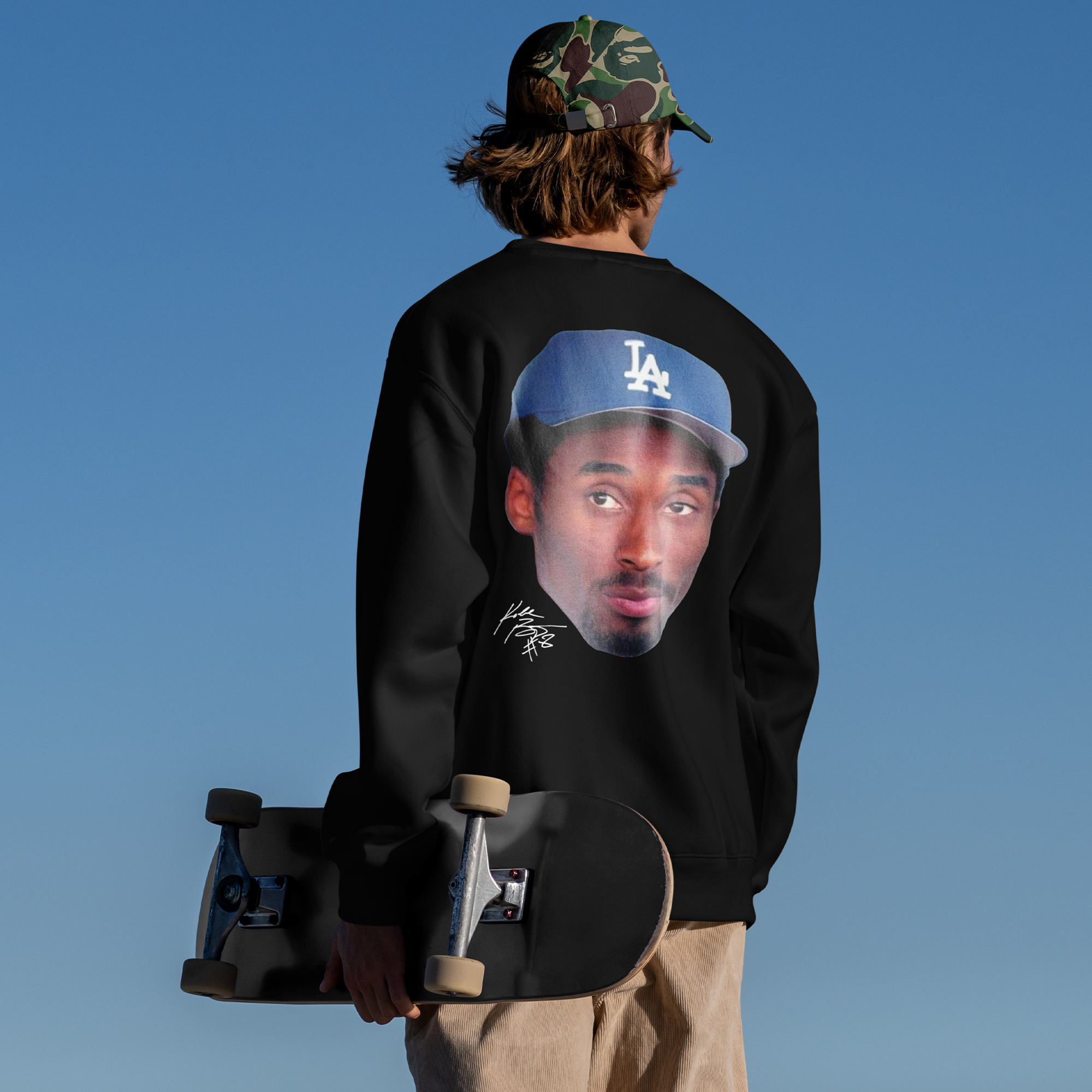 Person wearing a black sweatshirt with a graphic design, holding a skateboard against a clear blue sky.