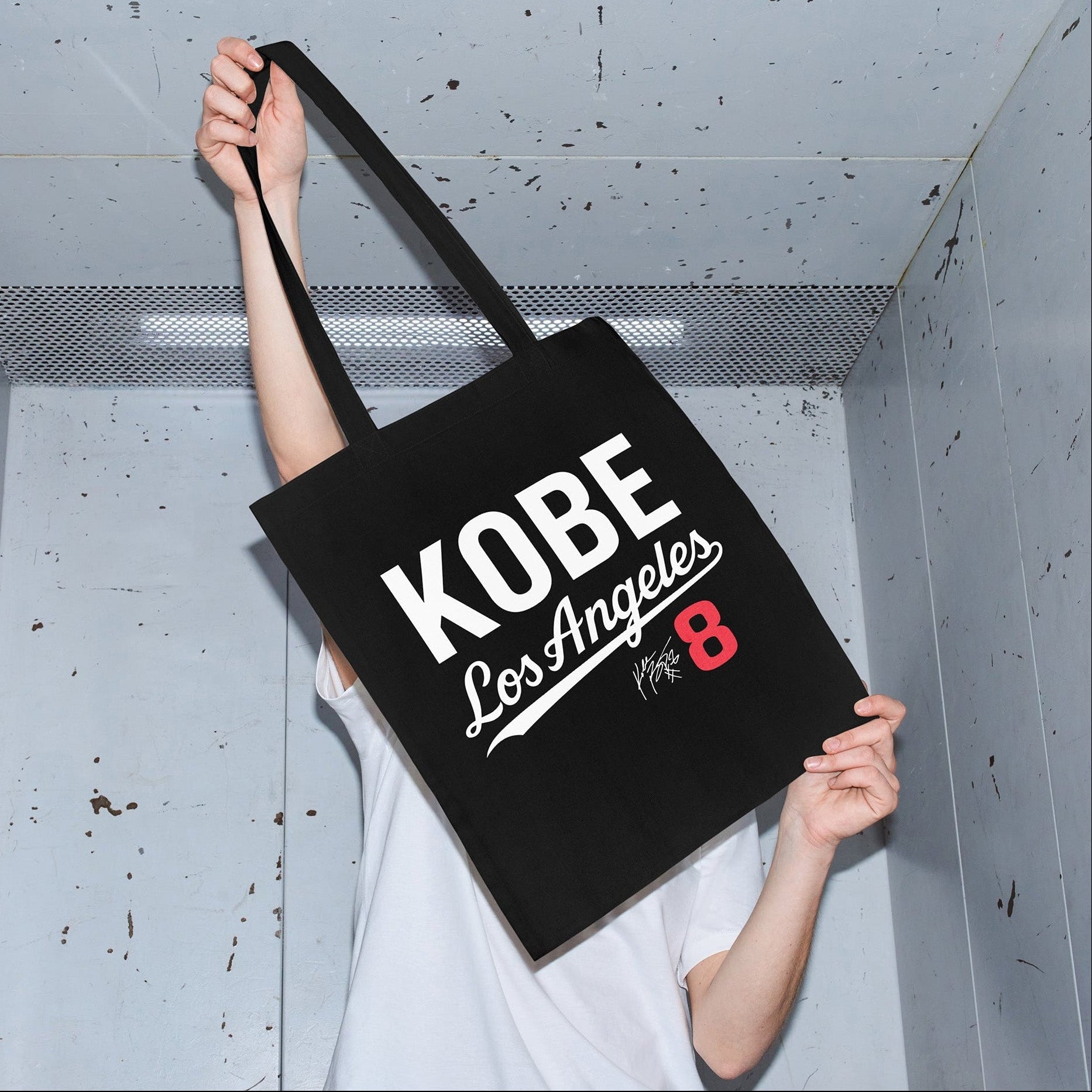 Person holding a black tote bag with 'Kobe Los Angeles 8' text in an elevator.