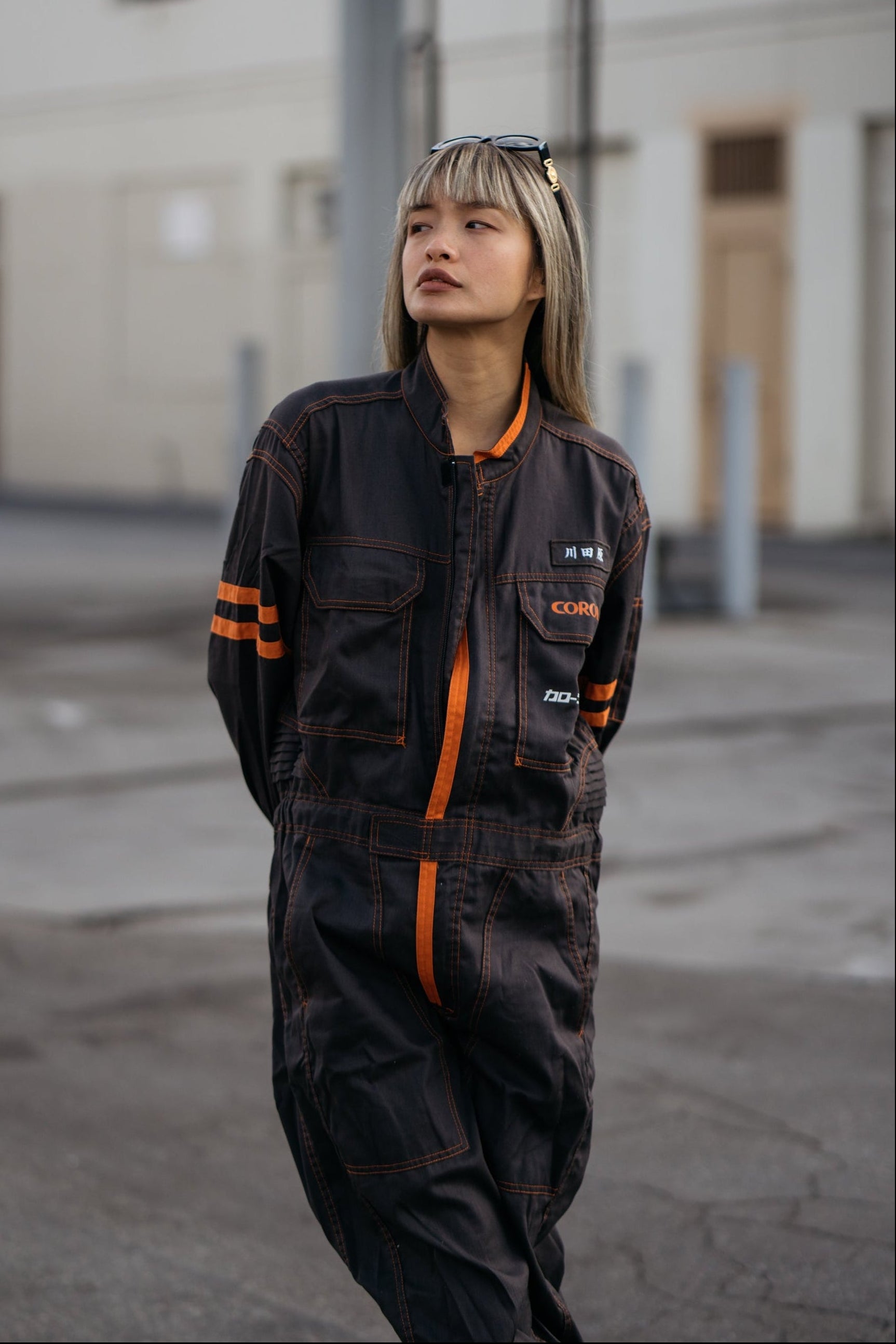 Person wearing a dark jumpsuit with orange accents standing in an urban setting.